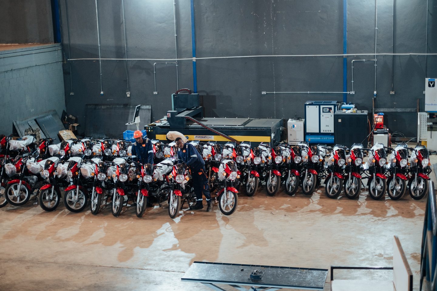 Workers with rows of red motorcycles and factory machinery.