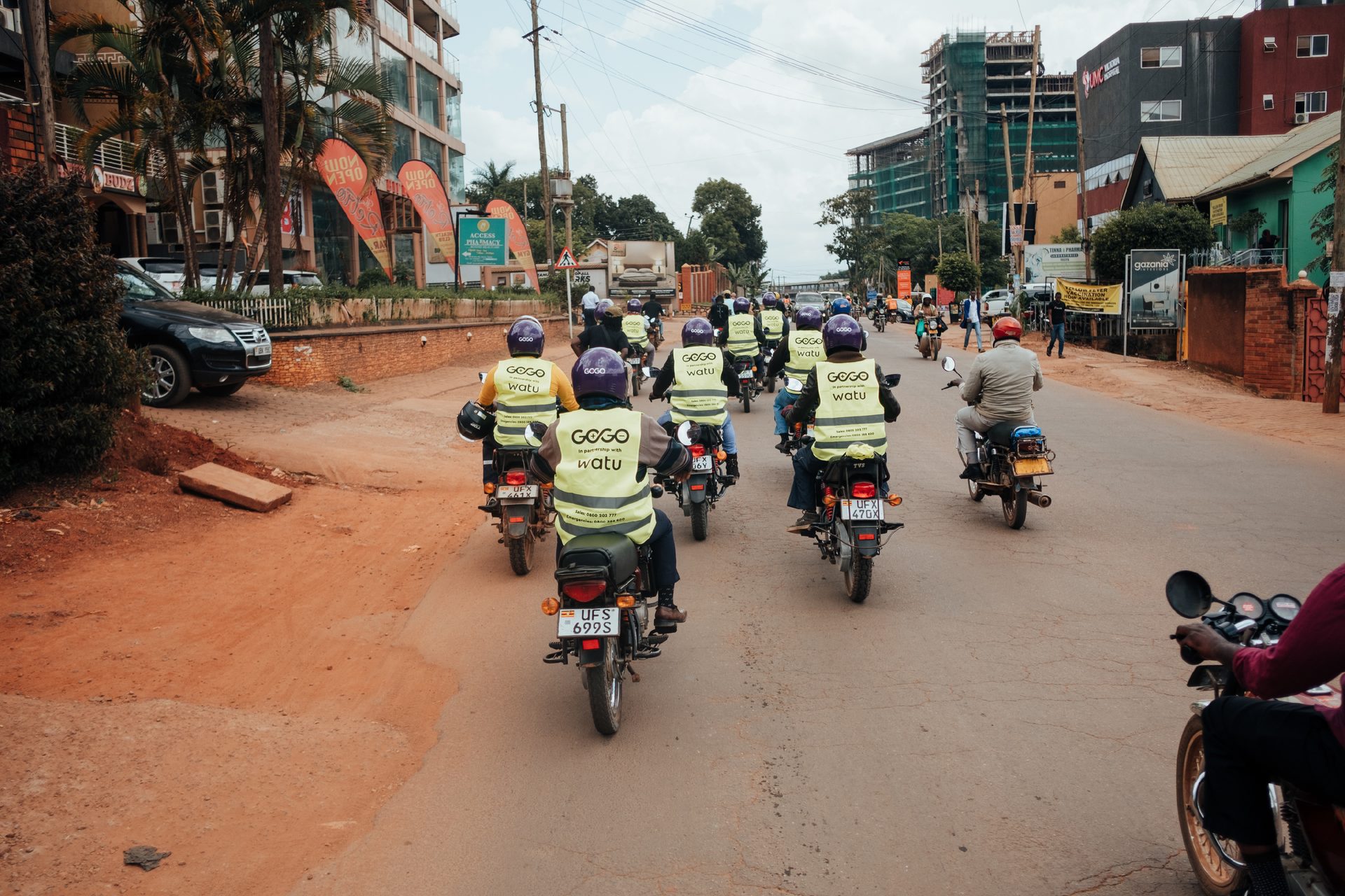 Group of motorcyclists wearing "GOGO watu" vests on an urban street.