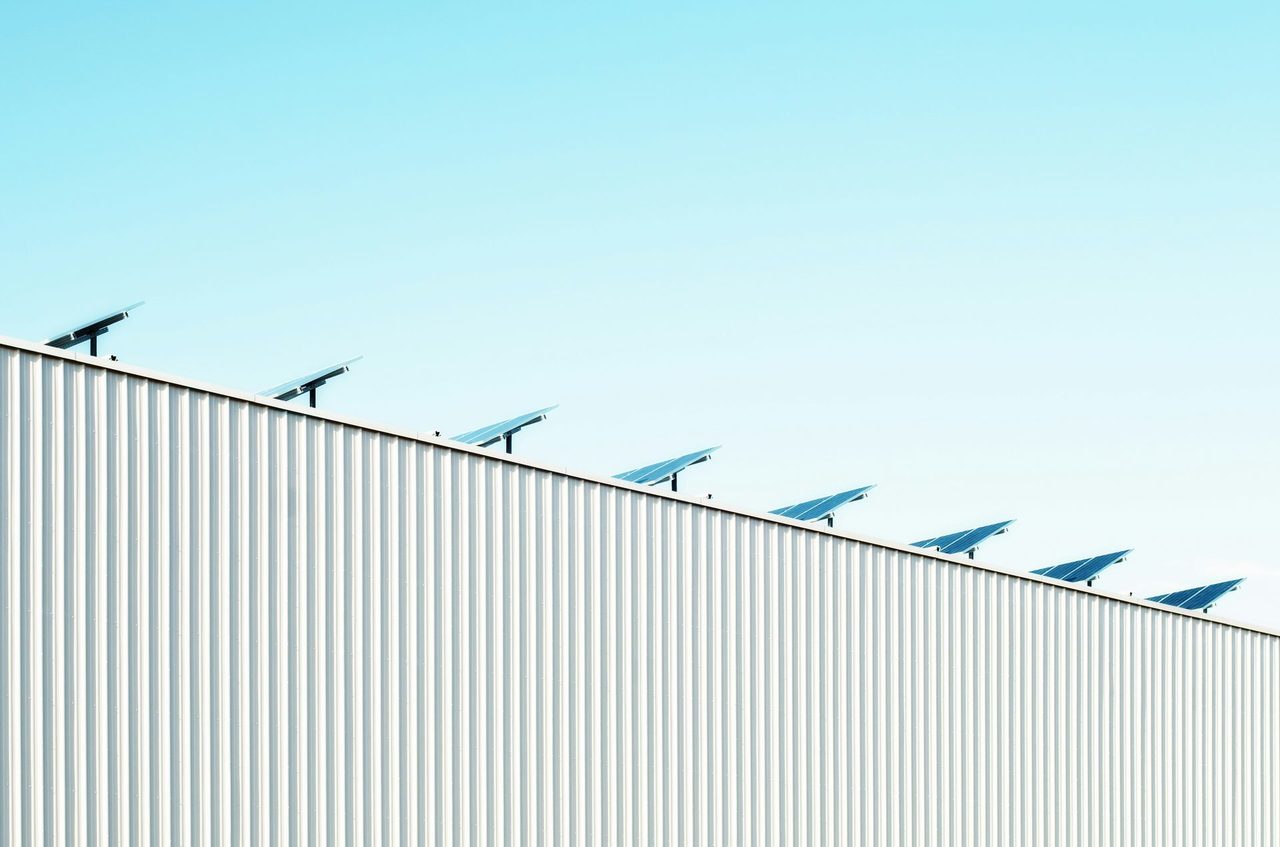 Row of solar panels on a white metal roof against a clear blue sky.