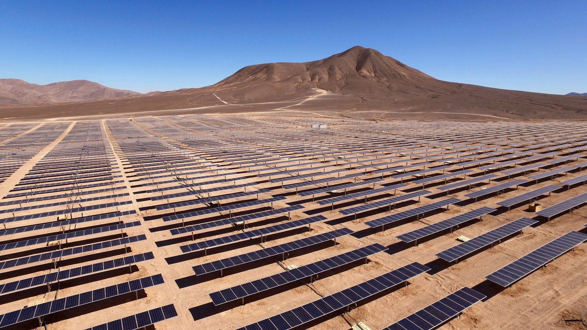 Aerial view of vast solar farm in desert landscape with mountains.